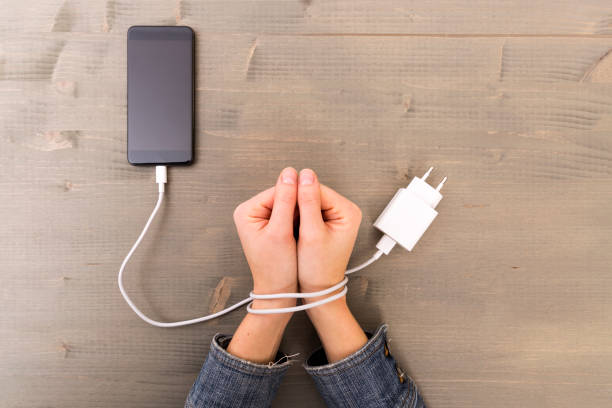 Female hands and smartphone. Woman's hands trapped and wrapped on wrists with mobile phone cable as handcuffs. Addiction to internet and social networks